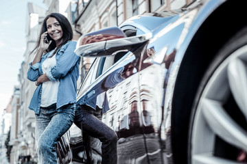 Plakat Distance communication. Positive nice happy woman leaning on her car and smiling while talking on the phone