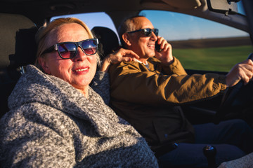 Portrait of smiling elderly couple driving car, while driver talking on phone.