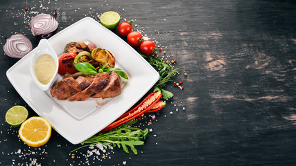 Pork steak with grilled vegetables on a plate. On a wooden background. Top view. Copy space.