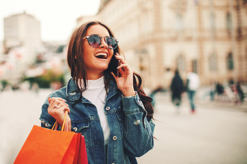 Fototapeta premium Beautiful young woman talking on the phone in the city after shopping