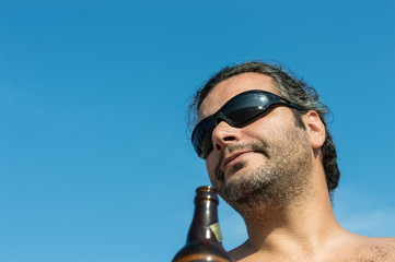 Portrait of a young happy Caucasian man with sunglasses enjoying a bottle of beer on a summer day.