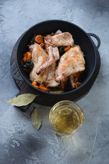 Cast-iron pan with rabbit stewed in white wine with prunes, carrots and onion, grey concrete background, high angle view