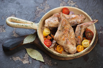 Frying pan with stewed rabbit and fresh cherry tomatoes, brown stone background, horizontal shot