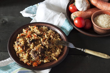 Plov and ingredients in a plate on a dark wooden background.