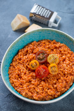 Risotto with tomatoes and parmesan cheese served in a blue bowl, vertical shot, selective focus
