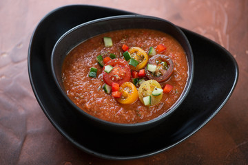 Black bowl with gazpacho tomato soup on a rusty metal background, studio shot, selective focus