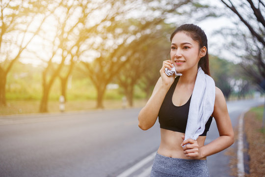 young sporty woman resting and wiping her sweat with a towel after workout sport exercises outdoors at park