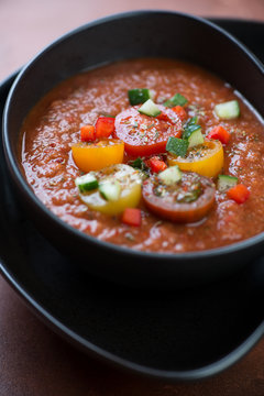 Close-up of cold gazpacho soup served in a black bowl, vertical shot, selective focus