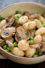 Closeup of boiled italian gnocchi with roasted mushrooms and green peas, selective focus, studio shot