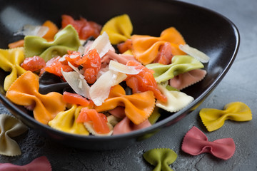 Closeup of a black bowl with multicolored farfalle, salmon and parmesan, selective focus, studio shot