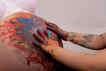 Bauch einer Schwangeren, der von den Händen eines Kleinkinds mit bunter Fingerfarbe eingerieben...