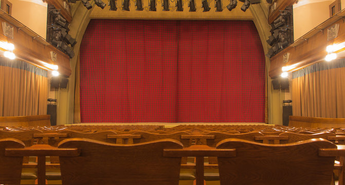 Theatre stage with closed curtain and empty wood seats