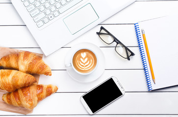 phone croissant coffee laptop view from above wooden white background
