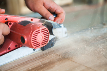 worker planing a table top of wood with a electric plane