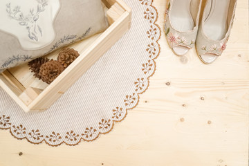 Fototapeta na wymiar A top view of a round lace carpet, pillow and pine cones in wooden box on a light wooden floor background, next to the high heels in a lady's room focus on the carpet. Cozy home interior concept.