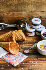 A Kit For Making Ice Cream: Spoon For Ice Cream, Ice Cream Cones, Jam, Topping, Chocolate, Sprinkles, Coconut Shavings. On Wooden Background. The Concept Of A Set, Surprise, Gift Idea
