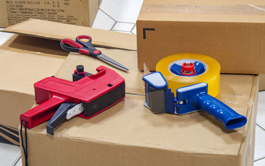 Packing tape dispenser, scissors and label gun on the cardboard box.