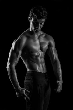 Highly retouched black and white fitness model and bodybuilder, Looking and posing abs and chest. concept of power and strength. black background.