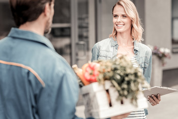 My order. Positive nice young woman smiling and looking at the delivery man while waiting for her delivery