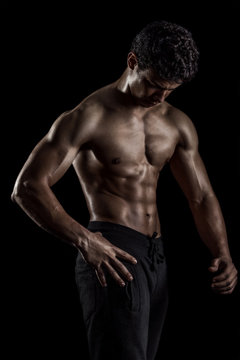 Highly retouched fitness model and bodybuilder. Looking to himself. Posing abs and chest. Concept of power, energy and self-confidence. black background.