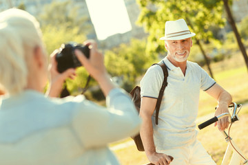 Active lifestyle. Joyful handsome aged man standing near his bike and smiling while posing for a photo