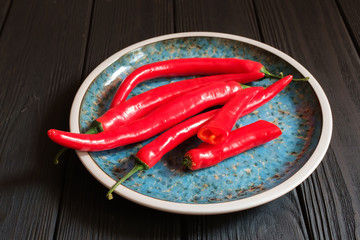 Red hot peppers in plate on dark wood.