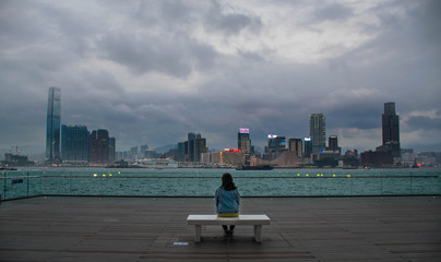 A girl on a bench looking at the Hong Kong skyline.
