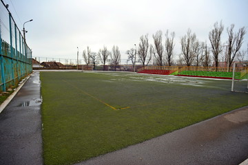 Puddles on a football field. White rusty gates and tribune without spectators.