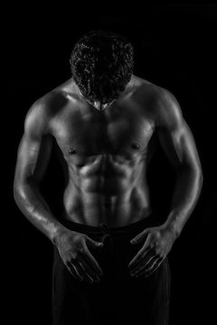 Highly retouched black and white fitness model and bodybuilder. Looking to himself. Posing abs and chest. Concept of power, energy and confidence. black background.