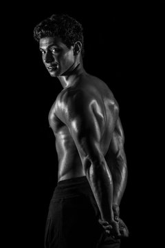 Highly retouched black and white fitness model and bodybuilder, Looking and posing triceps and back. Concept of power and strength. black background.