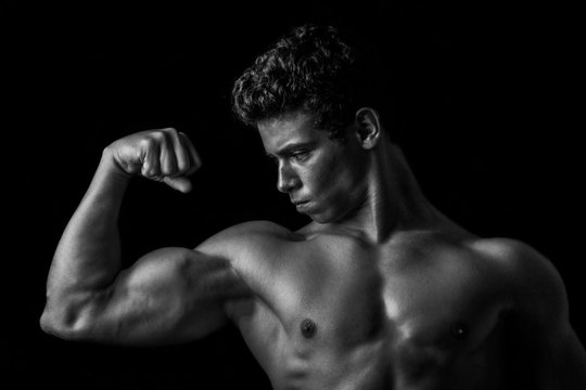 Highly retouched black and white fitness model and bodybuilder posing biceps. concept of strength. black background.