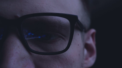 Man, face, with glasses, reflection, looking at graphics and work on the Internet, black background.	