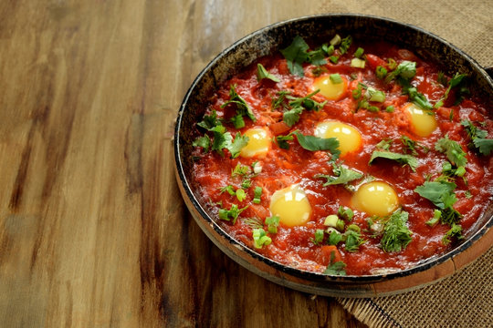 Fried eggs with tomato sauce in a cast iron pan. Shakshuka a traditional meal of the Jewish cuisine. Copy space