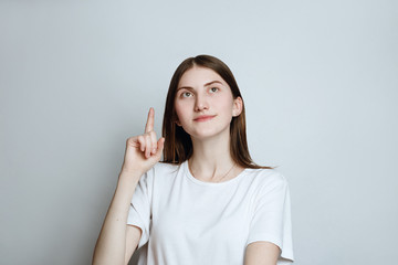 Model  in a t-shirt on a white background. The girl poses in studio, pointing fingers up with cheerful and happy expression of face