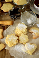 Shaped shortbread cookies covered with sugar powder surrounded by kitchen utensils