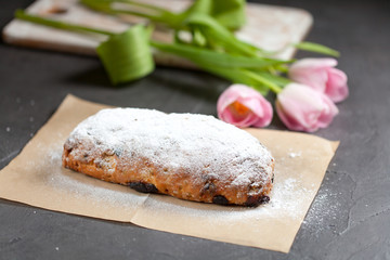 freshly baked cake with sweets, raisins and candied fruits, sprinkled with powdered sugar on a gray table with pink tulips