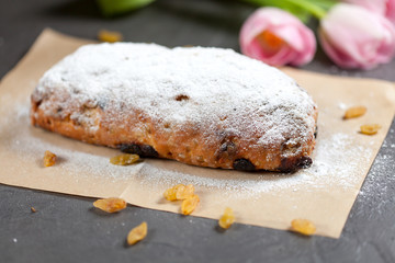 freshly baked cake with sweets, raisins and candied fruits, sprinkled with powdered sugar on a gray table with pink tulips