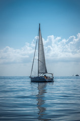Sailing boat on the sea sails reflect on a calm water summer day dark blue colors
