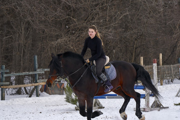 A girl on a horse  jumps  gallops. A girl trains riding a horse in a small paddock. A cloudy winter day.