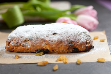 freshly baked cake with sweets, raisins and candied fruits, sprinkled with powdered sugar on a gray table with pink tulips