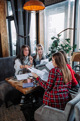 business meeting in a cafe, four young women sitting at a table and discussing documents