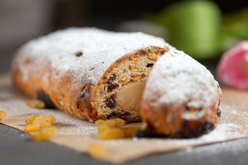 freshly baked cake with sweets, raisins and candied fruits, sprinkled with powdered sugar on a gray table with pink tulips