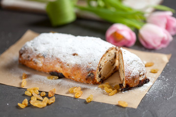 freshly baked cake with sweets, raisins and candied fruits, sprinkled with powdered sugar on a gray table with pink tulips
