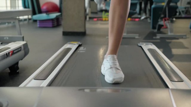 A close up of a woman running on a treadmill. White sneakers shoes sport. Female runner training fast athlete