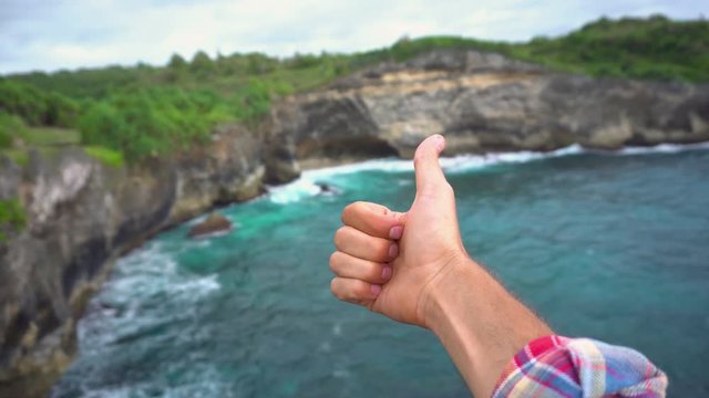 Man showing thumb up on beautiful landscape backgroung, high cliff, ocean waves