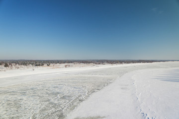 shot of snowy landscape with clear sky and frozen river
