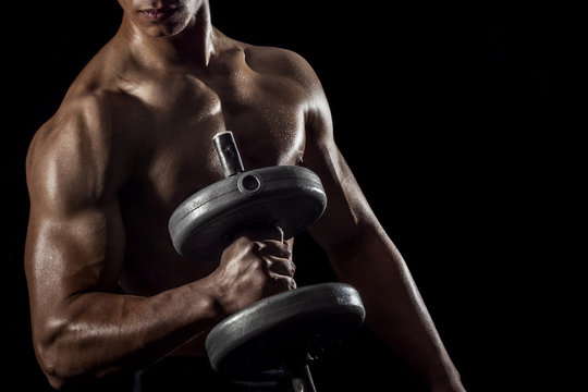 Highly retouched fitness model and bodybuilder training with dumbbells. posing the biceps and shoulder. concept of strength and power. black background.