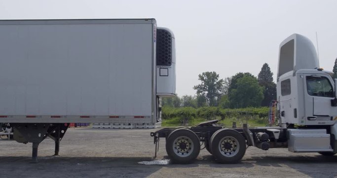 White truck cab pulls away, leaving unhitched white trailer on summer day in rural area. Side view, real-time 4K.