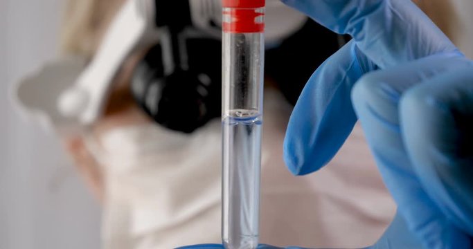 Laboratory work, a woman doctor holds a test tube, in a medical mask and professional glasses, a magnifying glass, takes an analysis from a test tube in blue rubber gloves, analysis, blood, DNA, a tes