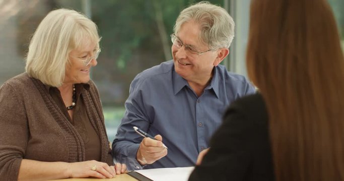 4K Happy senior couple in a meeting with estate agent signing contract & taking key to new home. Slow motion